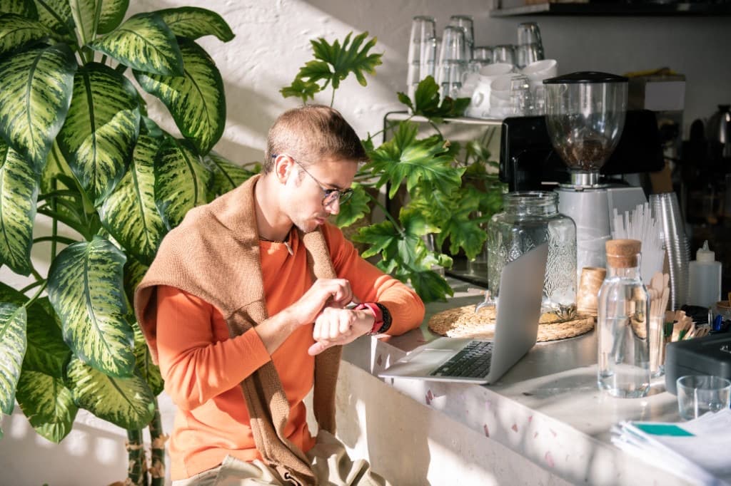 Homeowner checking a smartwatch beside an open laptop in a bright, plant-filled space