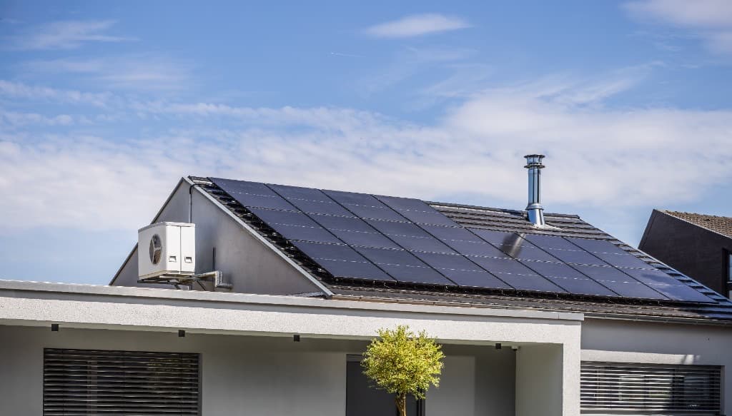 Modern home with rooftop solar panels and a wall-mounted outdoor heat pump unit